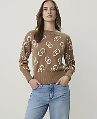 A woman in a tan sweater with a white interlocking ring pattern stands against a plain white background. carousel Product Image 1