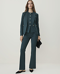 A woman in a teal pantsuit with gold buttons stands against a plain, light background, holding a black clutch. carousel Product Image 2