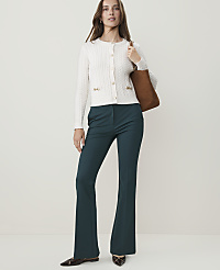 A woman in a white cardigan and teal flared pants stands against a plain, light background, carrying a brown tote bag. carousel Product Image 5