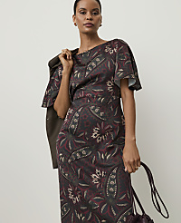 A woman in a patterned dress and jacket stands against a plain background, holding a handbag. carousel Product Image 3