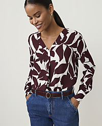 A woman in a floral blouse and jeans smiles with her hands in her pockets against a plain background. carousel Product Image 1