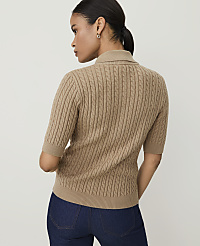 A woman in a tan cable-knit sweater and dark jeans stands against a plain beige background. carousel Product Image 2