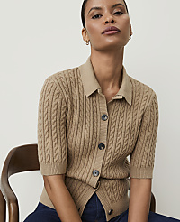 A woman in a cable-knit cardigan sits in front of a plain, light-colored background. carousel Product Image 3