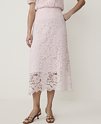 A woman in a light pink lace skirt and matching top stands against a plain white background, her feet adorned with brown heeled sandals. carousel Product Image 2