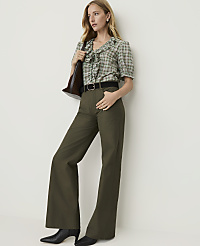 A woman in a green plaid blouse and olive green flared pants stands against a plain white background, holding a brown purse. carousel Product Image 1