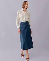 A woman in a white polka dot blouse and a denim skirt stands against a plain lavender background. carousel Product Image 4
