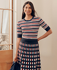 A smiling woman in a striped top and patterned skirt stands in a well-lit room with a doorway to her left. carousel Product Image 4