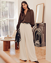 A woman in a brown blouse and cream wide-leg pants stands in a room with a fireplace and a round table. carousel Product Image 4