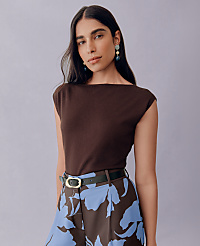 A woman with dark hair and large earrings stands against a plain purple background, wearing a brown top and patterned pants. carousel Product Image 3