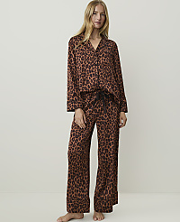 A woman in leopard print pajamas stands against a plain, light-colored background. carousel Product Image 1