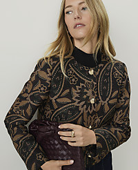 A blonde woman in a patterned jacket holds a woven clutch against a plain background. carousel Product Image 3