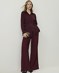 A woman in a burgundy pantsuit stands against a plain white background, holding a decorative clutch. carousel Product Image 4