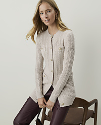 A woman in a cream cable-knit cardigan and burgundy pants sits on a wooden chair against a plain, light background. carousel Product Image 3