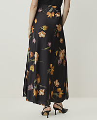 A person wearing a long, black floral skirt with orange and purple flowers stands against a plain, light-colored background. carousel Product Image 3