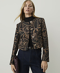 A woman in a patterned jacket and dark jeans stands against a plain, light background. carousel Product Image 1