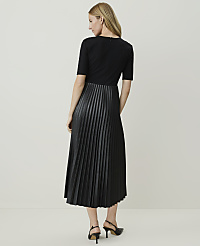A woman in a black dress with a pleated faux leather skirt stands against a plain, light-colored background. carousel Product Image 2
