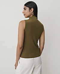 A woman in a sleeveless olive green turtleneck and white pants stands against a plain white background. carousel Product Image 2