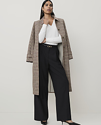 A woman in a white top, black wide-leg pants, and a plaid coat stands against a plain, light-colored background. carousel Product Image 5