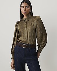 A woman in a patterned olive green blouse and dark jeans stands against a plain, light gray background. carousel Product Image 1