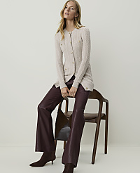 A woman in a cream cable-knit cardigan and burgundy leather pants sits on a wooden chair against a plain, light-colored background. carousel Product Image 4
