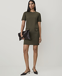 A woman in a green dress and brown slingback heels holds a woven brown clutch in front of a plain, light-colored background. carousel Product Image 1