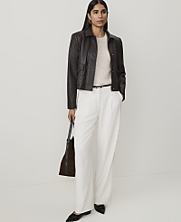 A woman in a cream sweater, dark brown leather jacket, and white wide-leg pants stands against a plain white background, holding a dark brown tote bag. carousel Product Image 1