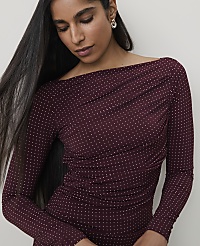 A woman with long dark hair and a sparkling maroon off-the-shoulder top is captured against a plain, light background. carousel Product Image 3