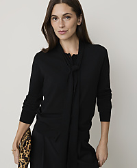 A woman in a black sweater with a bow detail holds a leopard-print clutch against a plain background. carousel Product Image 1