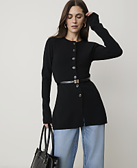 A woman in a black cardigan and light blue jeans stands against a plain white background, holding a black handbag. carousel Product Image 1