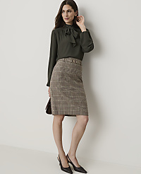 A woman in a dark green bow-neck blouse and a plaid pencil skirt stands against a plain, light-colored wall. carousel Product Image 4