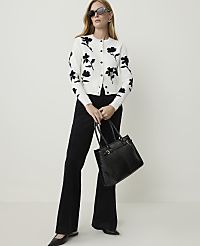 A woman in a floral cardigan and black flared pants poses with a black handbag against a plain white background. carousel Product Image 1