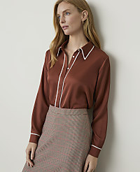 A woman in a rust-colored satin blouse and a patterned skirt stands against a plain, light-colored wall. carousel Product Image 1