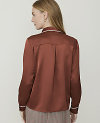A woman in a rust-colored satin shirt with white trim stands against a plain, light-colored background. carousel Product Image 2