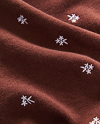 A close-up view of a rust-colored fabric with a subtle texture is adorned with small, white embroidered snowflake-like patterns scattered across its surface. carousel Product Image 2