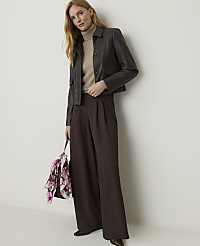 A woman in a brown leather jacket and wide-leg pants stands against a plain white background, holding a floral scarf. carousel Product Image 1
