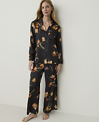 A woman stands in a black floral pajama set against a plain, light-colored wall. carousel Product Image 1