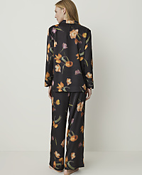 A woman stands facing away from the camera wearing black pajamas with a floral print, set against a plain white background. carousel Product Image 2