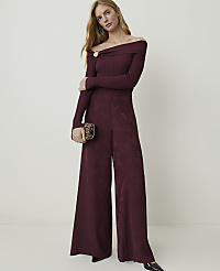A woman in a burgundy off-the-shoulder jumpsuit and patterned clutch stands against a plain, light-colored background. carousel Product Image 1