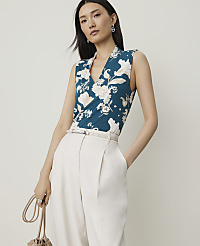 A woman in a teal floral top and cream pants stands against a plain, light background, holding a small, gathered bag. carousel Product Image 1