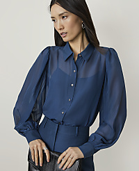 A woman in a sheer blue blouse and matching pants holds a black clutch against a plain background. carousel Product Image 1