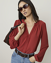A woman in a red blouse and jeans, wearing sunglasses and carrying a brown bag, stands against a plain background. carousel Product Image 1