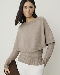 A woman in a beige sweater with a cape overlay stands against a plain, light background. carousel Product Image 1