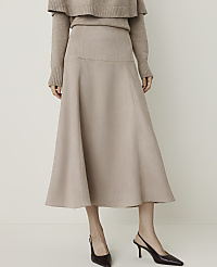 A woman in a beige sweater and a flowing beige skirt stands against a plain, light-colored background, wearing dark slingback heels. carousel Product Image 2