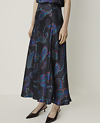 A woman in a flowing, dark skirt with a colorful paisley print stands against a plain, light-colored background. carousel Product Image 2