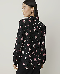 A woman in a black floral shirt stands against a plain, light gray background. carousel Product Image 2