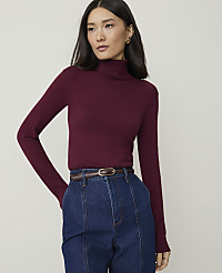 A woman in a burgundy turtleneck and blue jeans stands against a plain gray background. carousel Product Image 1