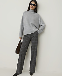 A woman in a grey turtleneck sweater and plaid pants stands against a plain white background, holding a brown bag. carousel Product Image 4