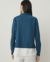 A woman in a teal mock-neck top and white pants stands against a plain, light background. carousel Product Image 2