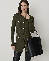 A woman in a brown cable-knit cardigan and black pants stands with a black tote bag in front of a plain, light-colored background. carousel Product Image 1