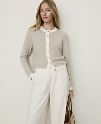 A woman in a beige cardigan and white pants stands against a plain, light-colored background, holding a brown tote bag. carousel Product Image 1